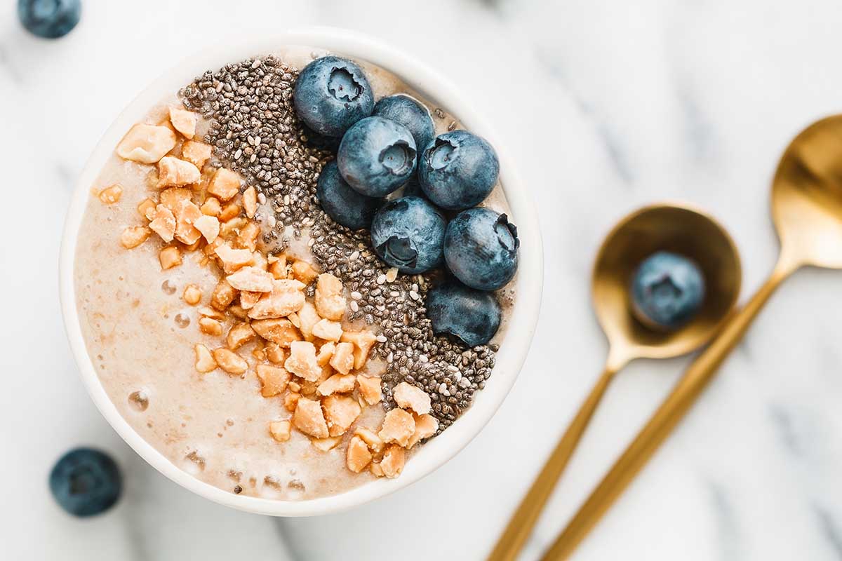 Top view of a smoothie bowl with fresh ripe blueberry, nuts, chia, banana and soya milk over white background. The concept of healthy eating and lifestyle.