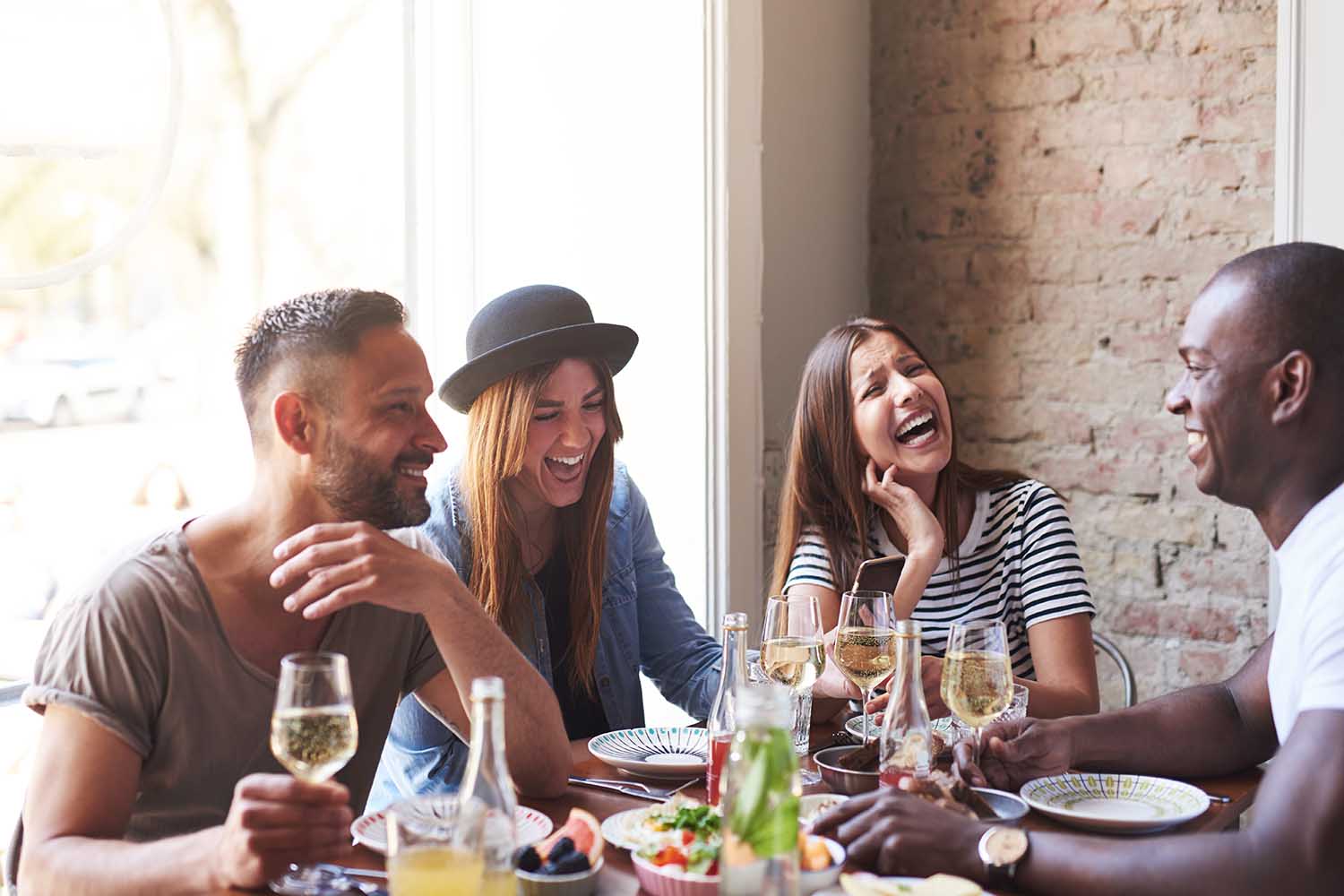 Group of young friends having fun and laughing while dining at table in restaurant.