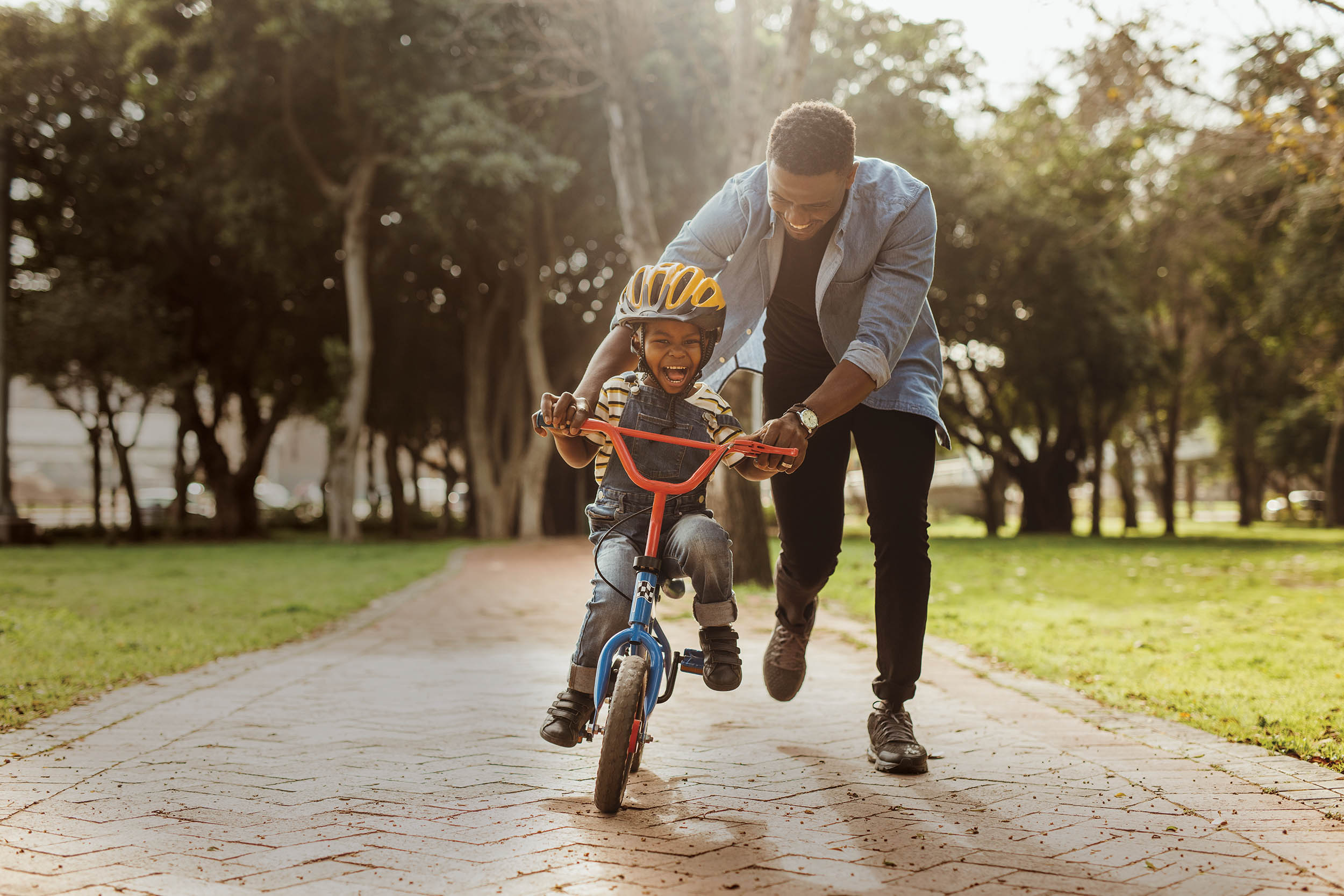 Boy learning to ride a bicycle with his father in park. Father teaching his son cycling at park.
