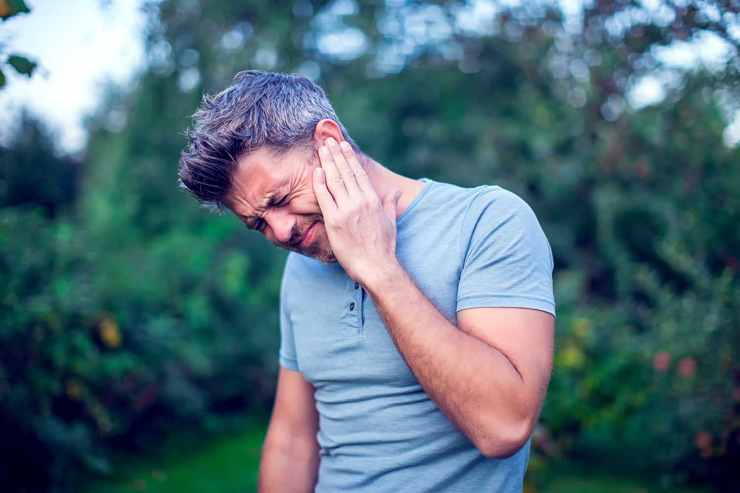 Unhappy man having ear pain touching his painful head outdoor