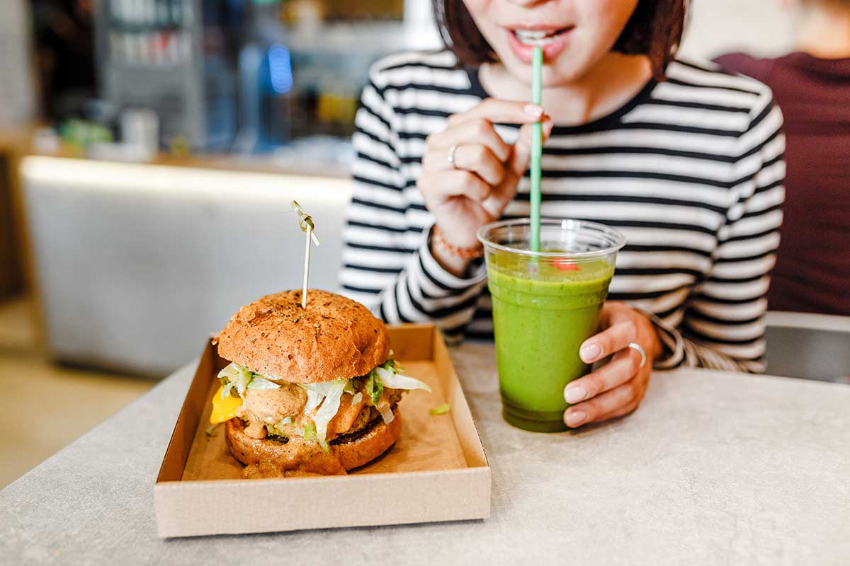 A young woman drinks green smoothies and eats a burger in a vegan fast food restaurant